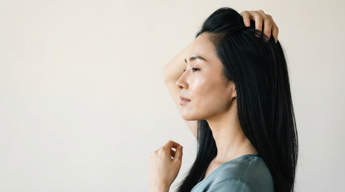 Donna di profilo con capelli lisci scuri che passa le dita tra le radici appena lavate